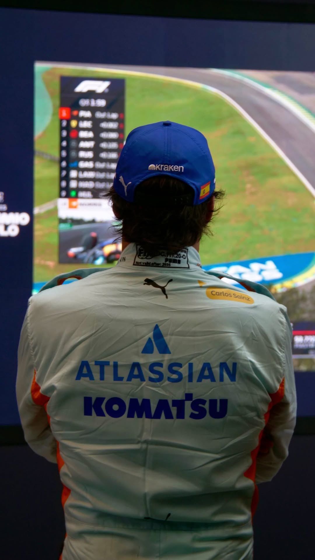Back View of Carlos Sainz wearing a light blue 2025 Williams Sao Paul GP F1 racing suit with 'ATLASSIAN KOMATSU' branding - GPX WEAR