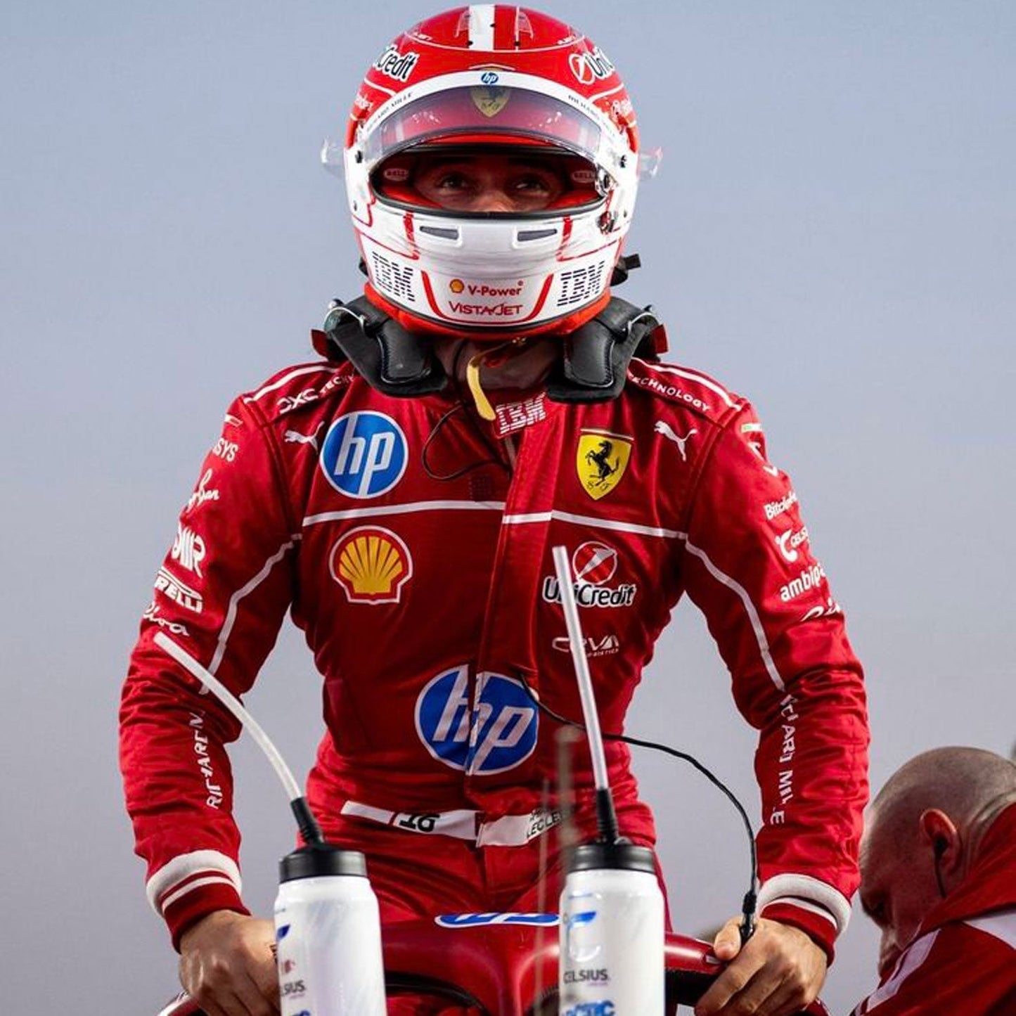 Charles Leclerc wearing a red 2025 Ferrari F1 racing suit with various sponsor logos, including HP and Ferrari, on a gray background - GPX WEAR