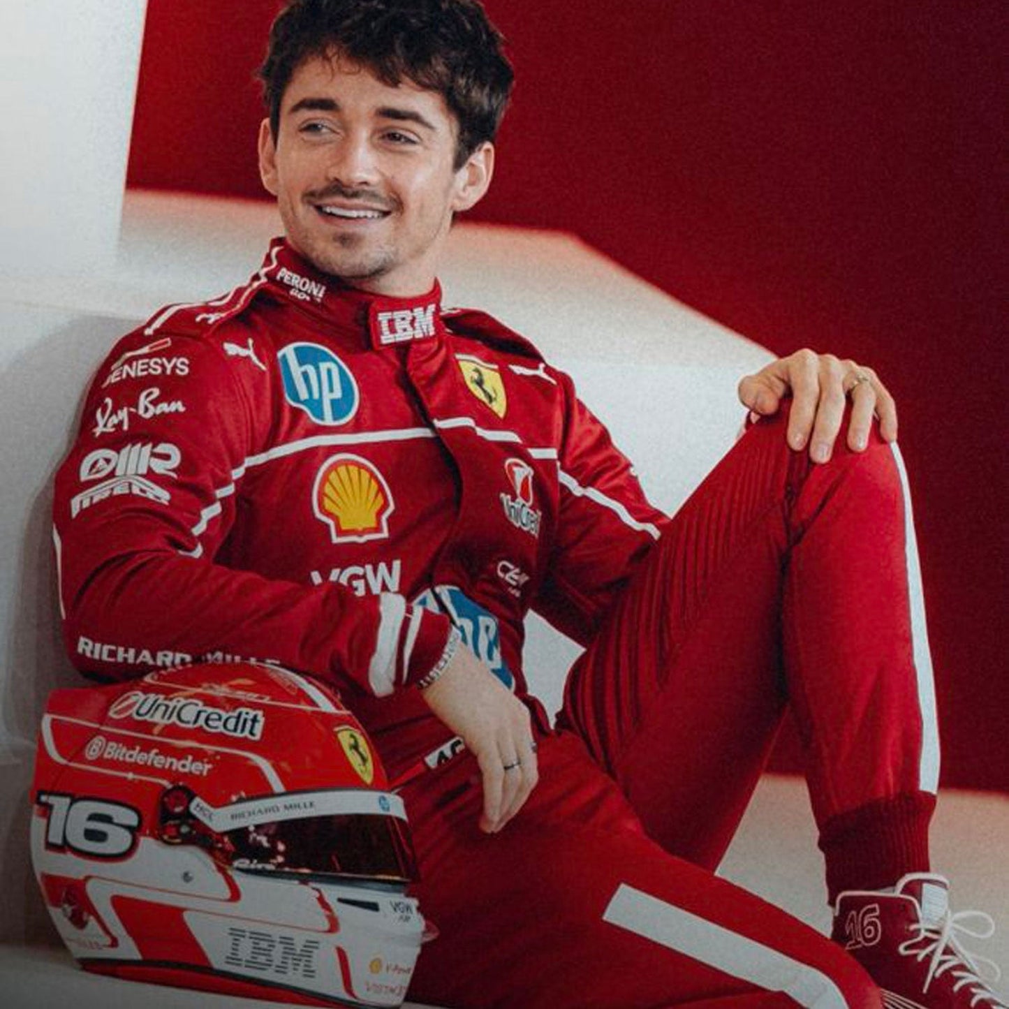 Charles Leclerc is wearing a red 2025 Ferrari F1 racing suit with various sponsor logos, sitting next to a helmet - GPX WEAR