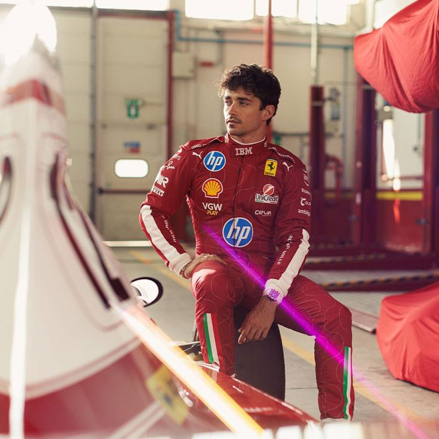 Charles Leclerc wearing a red 2025 Ferrari Monza GP F1 racing suit with multiple sponsor logos in a garage setting  - GPX WEAR