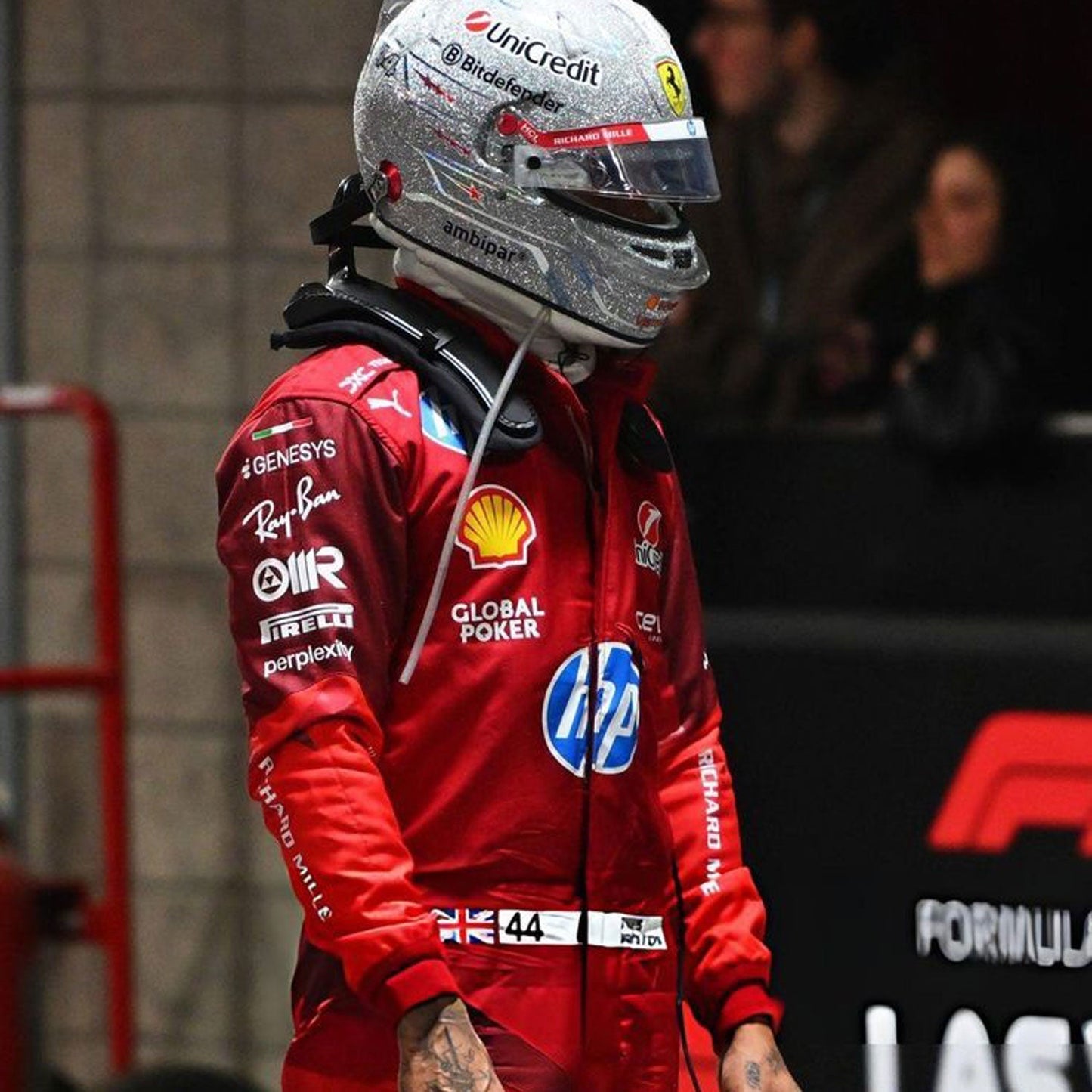 Lewis Hamilton wearing a red 2025 Ferrari Las Vegas GP F1 racing suit  with various sponsor logos, wearing a helmet with a Ferrari logo - GPX WEAR
