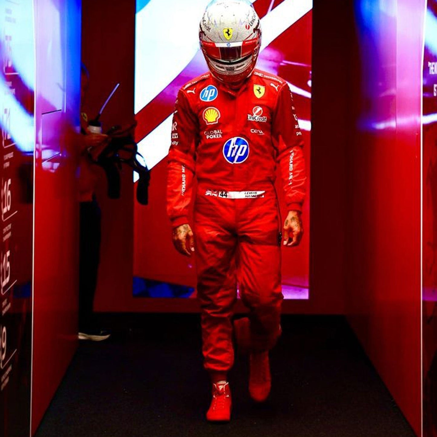 Lewis Hamilton wearing a red 2025 Ferrari Las Vegas GP F1 racing suit  with various sponsor logos in a red-themed room - GPX WEAR