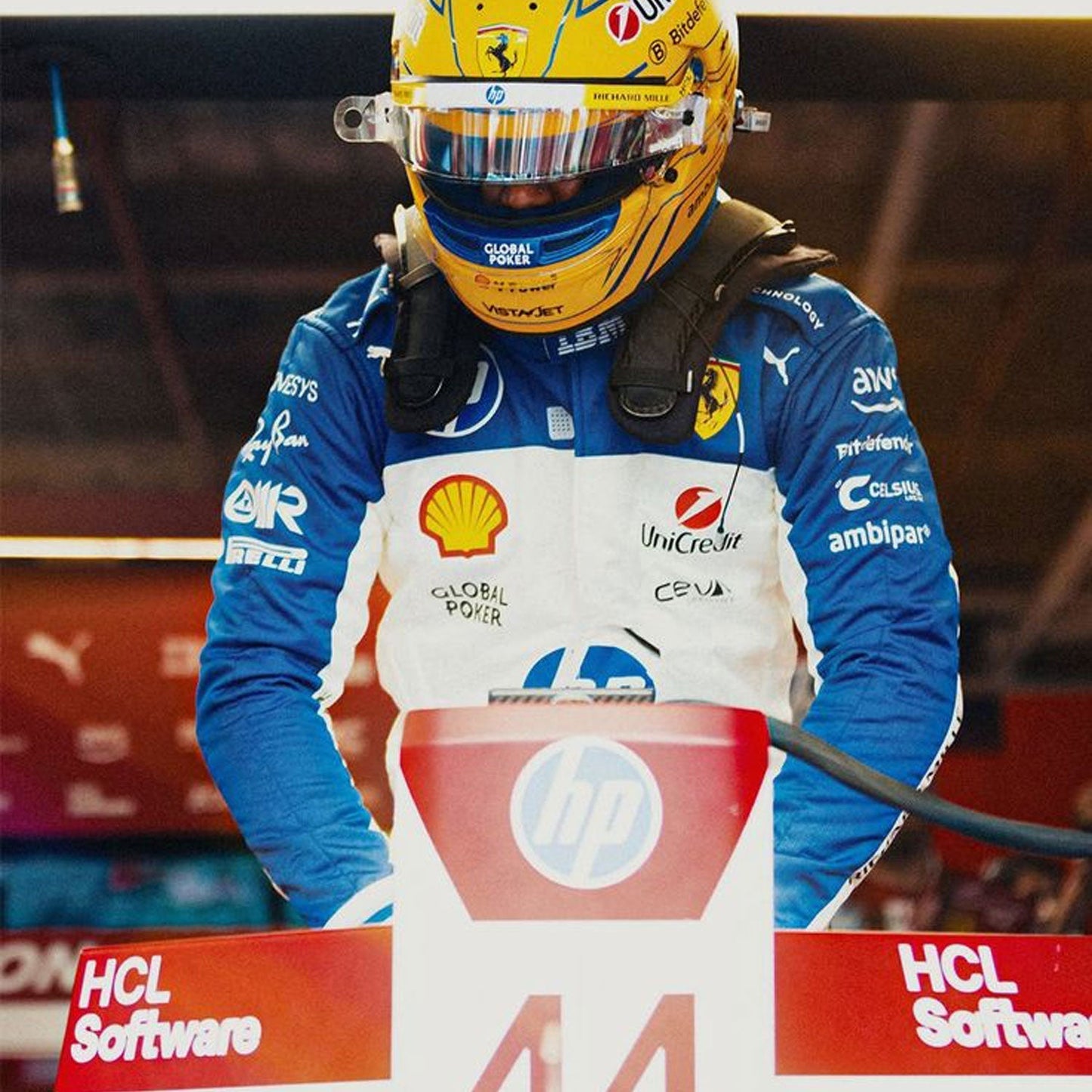 2025 Lewis Hamilton Miami GP F1 Racing Suit with various sponsor logos, standing on a pit stop platform.