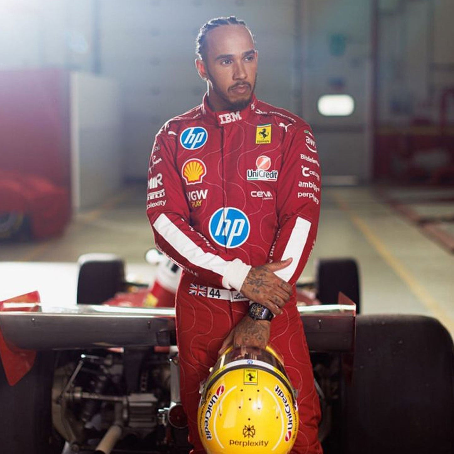 Lewis Hamilton wearing a red 2025 Ferrari Monza GP F1 racing suit with various sponsor logos, standing next to a Formula 1 car - GPX WEAR