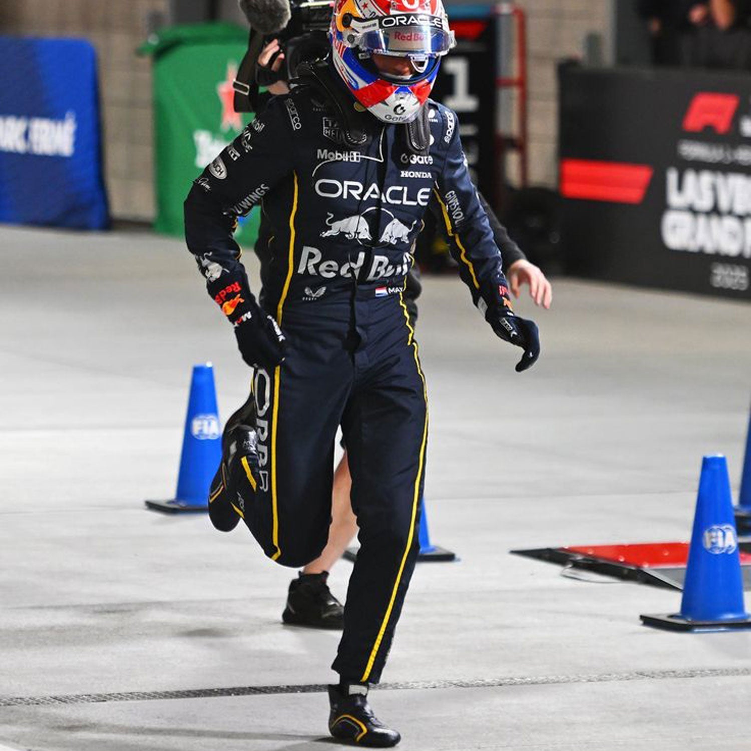 Max Verstappen wearing a black 2025 Red Bull Las Vegas GP F1 racing suit and helmet walking on a track with branding visible - GPX WEAR
