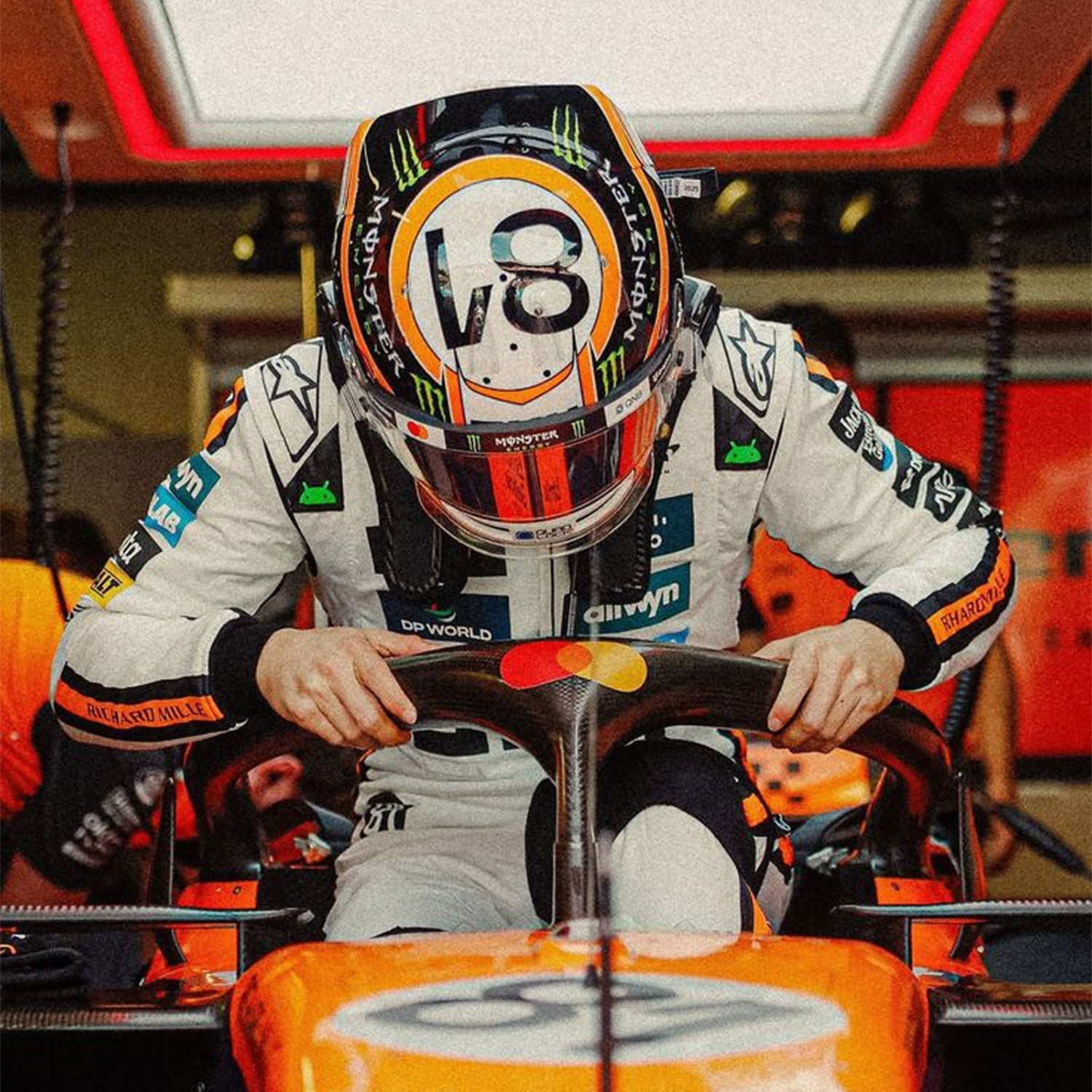 2025 Oscar Piastri Monaco GP F1 Racing Suit and helmet sitting in a Formula 1 car inside a garage.