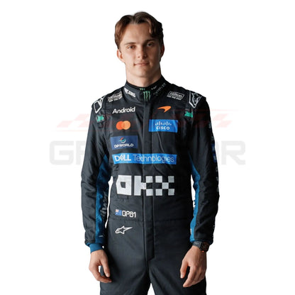 A Oscar Piastri wearing a black long-sleeve racing suit with multiple colorful sponsor logos, photographed against a plain white background.