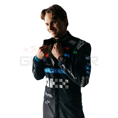 A Oscar Piastri wearing a black long-sleeve racing suit with multiple colorful sponsor logos, photographed against a plain white background.