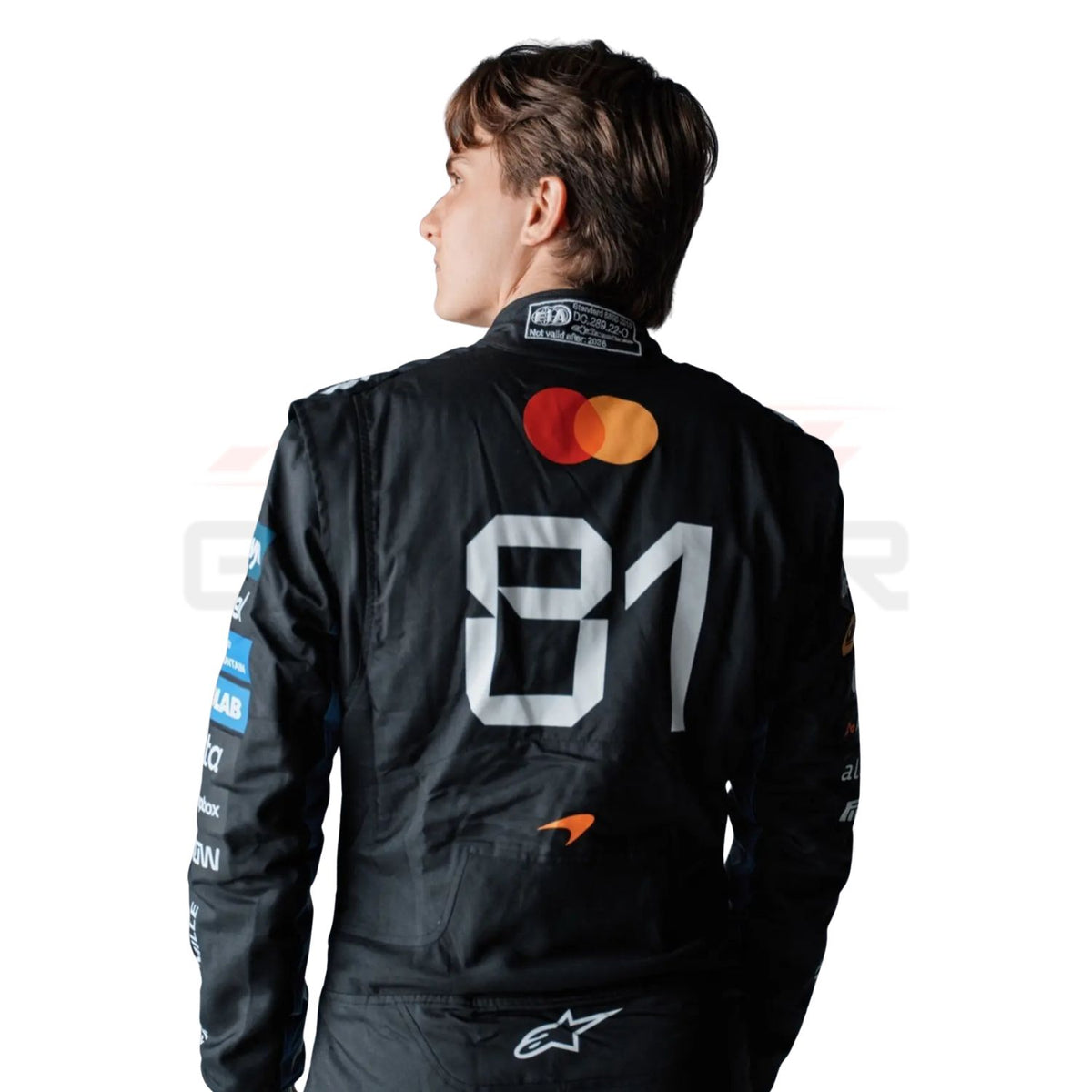 A Oscar Piastri wearing a black long-sleeve racing suit with multiple colorful sponsor logos, photographed against a plain white background.