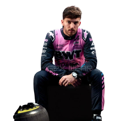 Pierre Gasly wearing a pink and black racing suit with visible branding, sitting on a racing tire